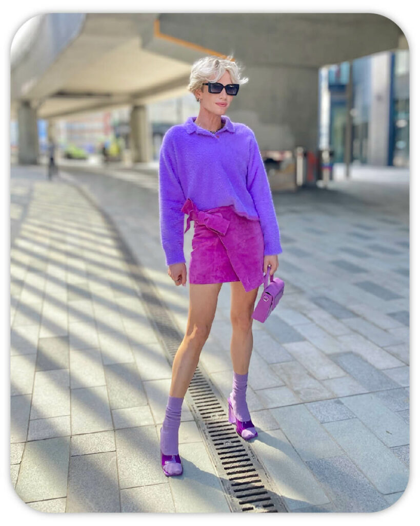 Photo of Danny Jennings, a Personal Stylist, in London wearing a purple polo jumper, fuchsia suede skirt, purple socks and matching heeled mules with sunglasses